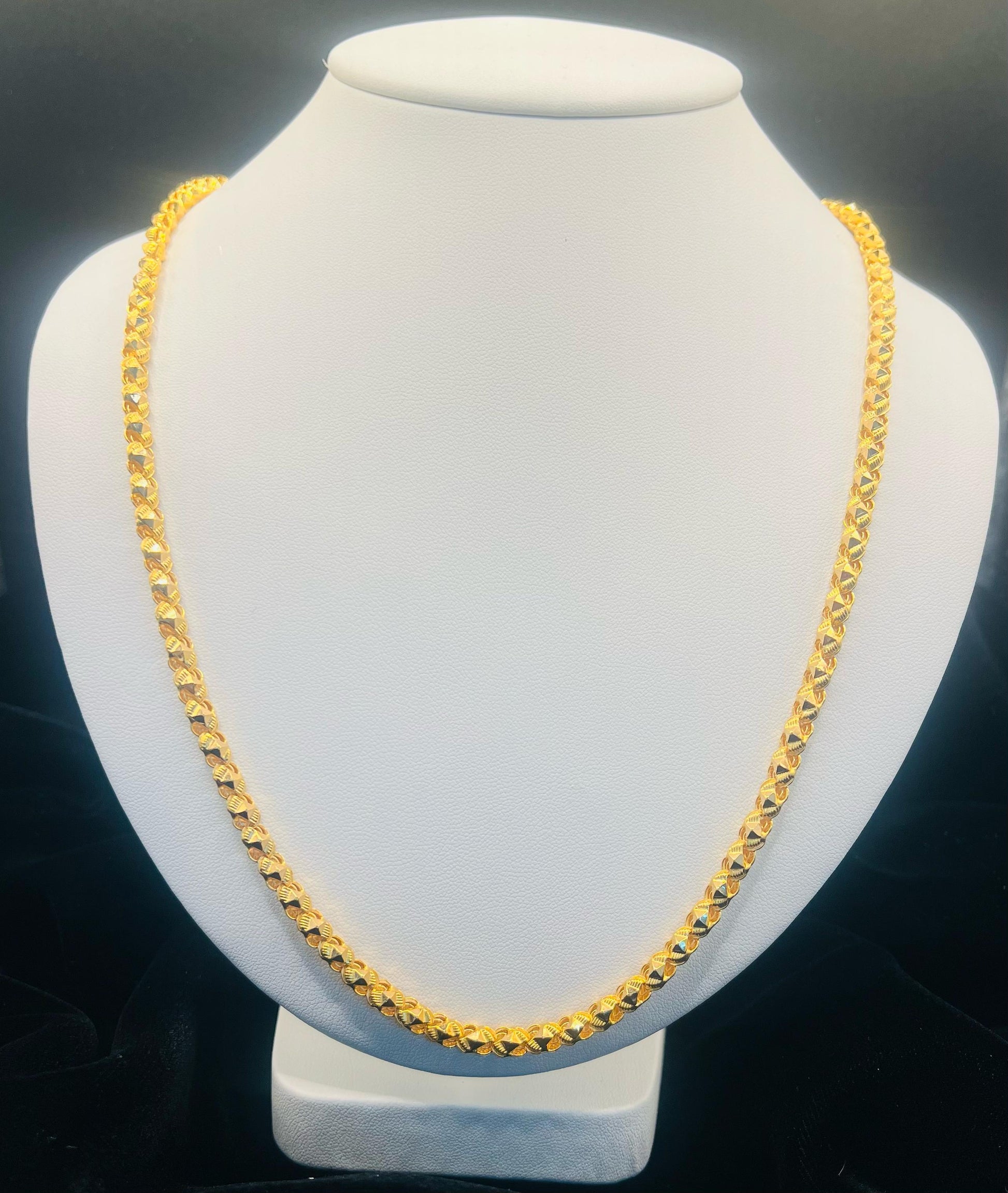 A gold-toned chain necklace displayed on a white jewelry bust against a dark background.